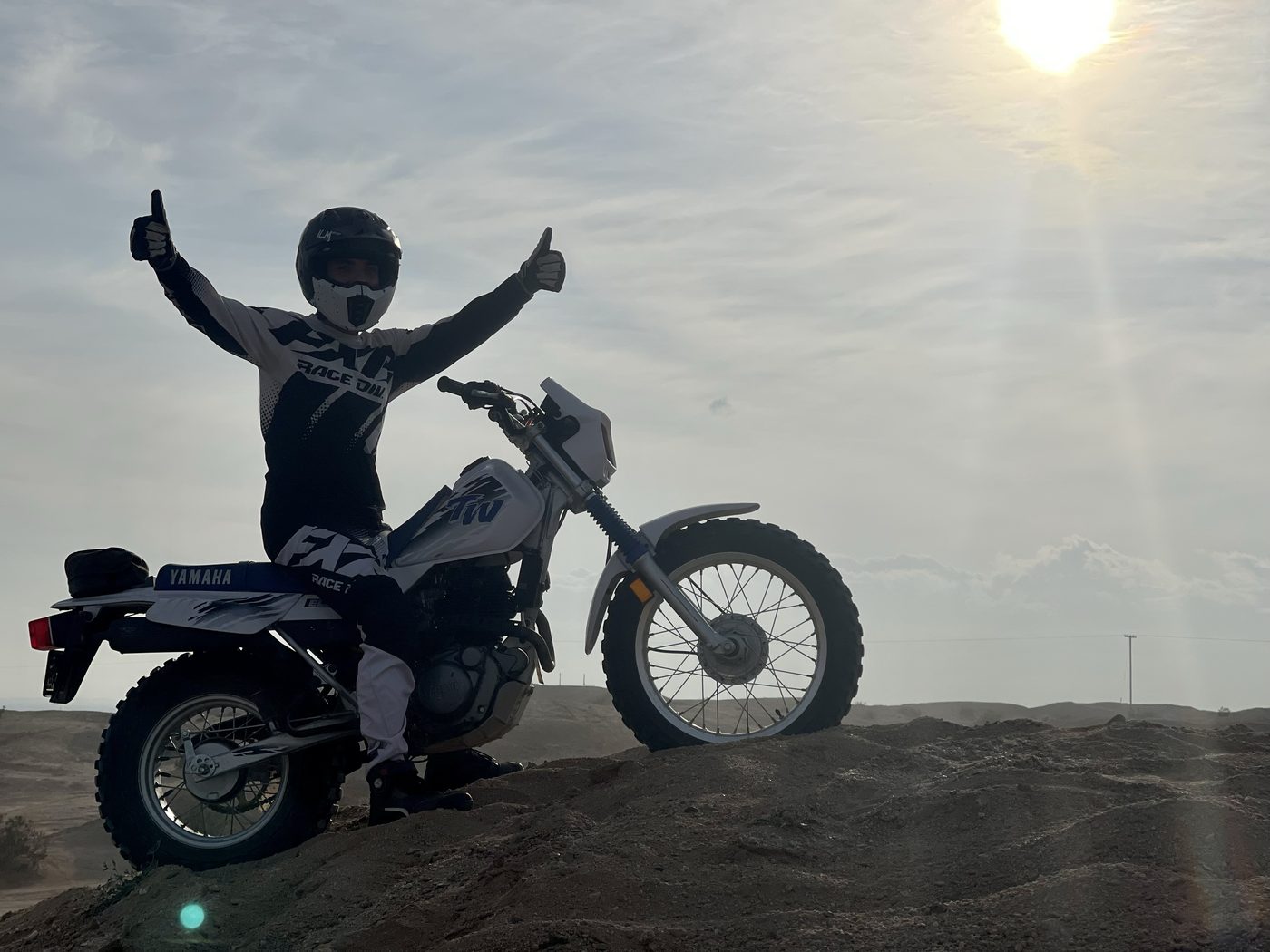Trent giving a thumbs up on a Yamaha dirt bike on top of a sand dune